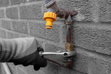 Wall Mural - Man replacing burst copper water pipe outdoors. Unscrewing a brass connector with a spanner wrench. With selective colour