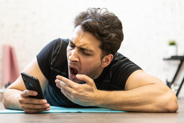 Wall Mural - Tired young man yawning while training on the floor at home. Do sport and exercise at the morning time concept