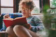 © simona - Woman at home sitting and reading a book in relax indoor leisure activity at home. Serene female people studying and read novel. Wearing glasses. Single lady lifestyle. Sunday time and vacation