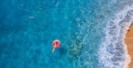 Concept tropical paradise travel relax. Aerial top view young woman swimming with donut pink inflatable swim ring in blue sea