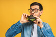 Young man holding a piece of sandwich. Student eats fast food. Burger is not helpful food. Very hungry guy. Diet concept. Isolated over yellow background.