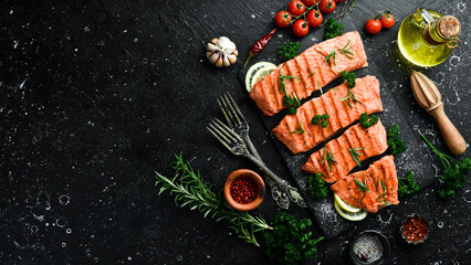 Wall Mural - Grilled trout fillet with spices, lemon and vegetables. On a black background.