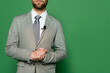 © LIGHTFIELD STUDIOS - Cropped view of news presenter in suit and clip microphone standing on green background