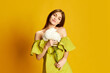 © master1305 - Portrait of young beautiful girl in cute dress posing with flowers over yellow background. Delightful