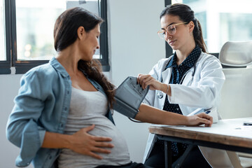 Female gynecologist checking the blood pressure of her pregnant patient in the clinic.