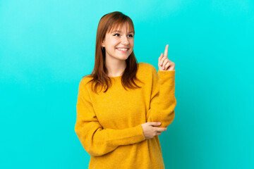 Wall Mural - Redhead girl isolated on blue background pointing up a great idea