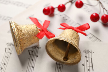 Wall Mural - Golden shiny bells with red bows and decorative berries on music sheets, closeup. Christmas decoration