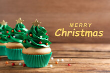 Greeting Card With Phrase Merry Christmas. Festively Decorated Cupcakes On Wooden Table