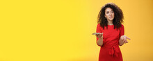 So Waht, I Confused. Questioned Uncertain Woman With Curly Hair In Red Dress Shrugging Looking Clueless As Holding Hand Cannot Understand Where Order As Checking Mail Box Via Device Over Yellow Wall