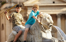 Portrait Of Two Children On Lion Statue At Fontana Dell'Obelisco, Piazza Del Popolo (People's Square) On Summer Vacation, Rome, Lazio, Italy