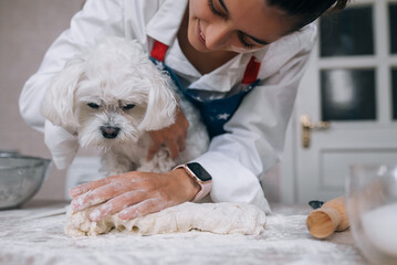 Woman in the kitchen kneads the dough with her dog