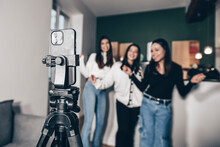 Close-up Of A Smartphone On A Tripod Filming 3 Young White Girls Dancing, At Home. Concept Of Making A Living With Videos On The Internet By Being An Influencer. Popularity And Celebrity Online