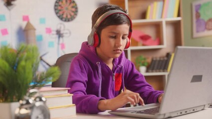 Serious teenager kid with headphones working laptop on study table at home - concept of intelligence, education and smart.