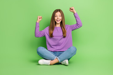 Poster - Full size photo of nice positive impressed girl with long hairstyle dressed jeans clenching fists isolated on green color background