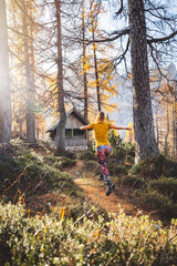 Canvas Print - Vertical photo view from the back of woman hiker jumping in the forest while on a hike on a sunny autumn day