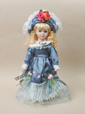 Fototapeta Sypialnia - Vintage porcelain doll baby girl with blue eyes, blonde curls, wearing a blue hat decorated with red flowers and a blue satin dress.