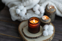 Cozy Autumn Or Winter Composition With Aromatic Candle, Wool Sweater, Cotton, Book. Aromatherapy, Home Atmosphere Of Cosiness And Relax. Wooden Background Close Up.