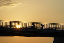 Sunset Over The Bridge And Silhouettes Of People Cycling And Running