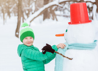 Wall Mural - Young boy playing with a snowman on a winter walk in nature