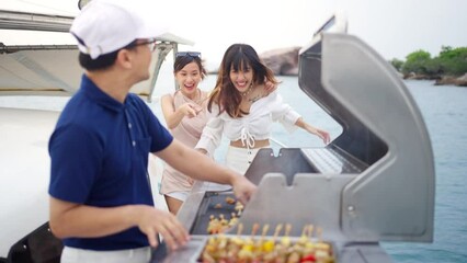 Wall Mural - 4K Asian man chef cooking grilled barbecue and seafood on stove for serving to woman passenger tourist travel on luxury private catamaran boat yacht sailing in the ocean on summer holiday vacation.