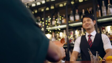 Poster - Asian man bartender preparing cocktail drink in cocktail glass serving to customer on counter at luxury restaurant bar. Barman making mixed alcoholic drink for celebrating holiday party at nightclub.