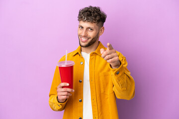 Wall Mural - Young blonde man holding soda isolated on purple background pointing front with happy expression