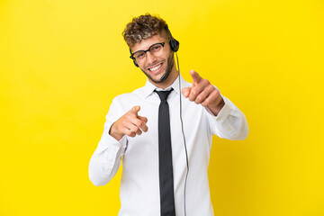 Wall Mural - Telemarketer blonde man working with a headset isolated on yellow background points finger at you while smiling