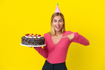 Wall Mural - Blonde Uruguayan girl holding birthday cake isolated on yellow background with surprise facial expression