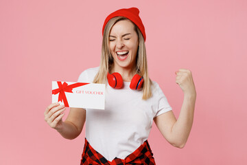 Wall Mural - Young happy fun woman wear white t-shirt red hat hold gift certificate coupon voucher card for store do winner isolated on plain pastel light pink background studio portrait. People lifestyle concept.