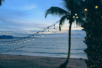 light bulbs on string wire decoration at the party event festival on the beach at sunset. Outdoor holiday background. Copy space.