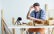 © Ann Rodchua - Senior old Caucasian man wearing check shirt, apron, making DIY wooden furniture, using mobile phone, streaming live video clip, selling product in social media at home. Retirement, Hobby Concept.