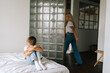 © dikushin - Angry young mother leaving the children room after after quarrel with sad crying little child daughter sitting on bed hugging knee, cover face at home. Concept of family problems, conflict, crisis.