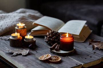 Cozy autumn or winter composition with aromatic candle, wool sweater, book. Aromatherapy, home atmosphere of cosiness and relax. Wooden background close up.