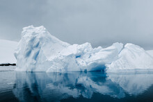 Iceberg Floating Off Enterprise Island In The Antarctic, With Mirror. Reflection In The Southern Ocean, With Winter Colors Of Grey, White, And Blue. 