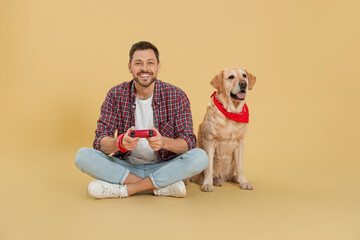 Sticker - Happy man playing game with controller near his cute Labrador Retriever on beige background