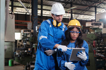 Two industrial workers in safety uniforms and hardhats, male manager, and Black colleague work with tablet to check metalwork machines in manufacturing factory. Professional production engineer team.