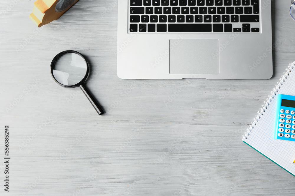 Modern laptop and magnifying glass on grey wooden table. Finance trading