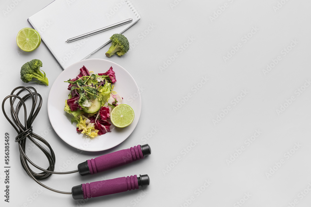 Plate with vegetable salad, skipping rope and notebook on grey background