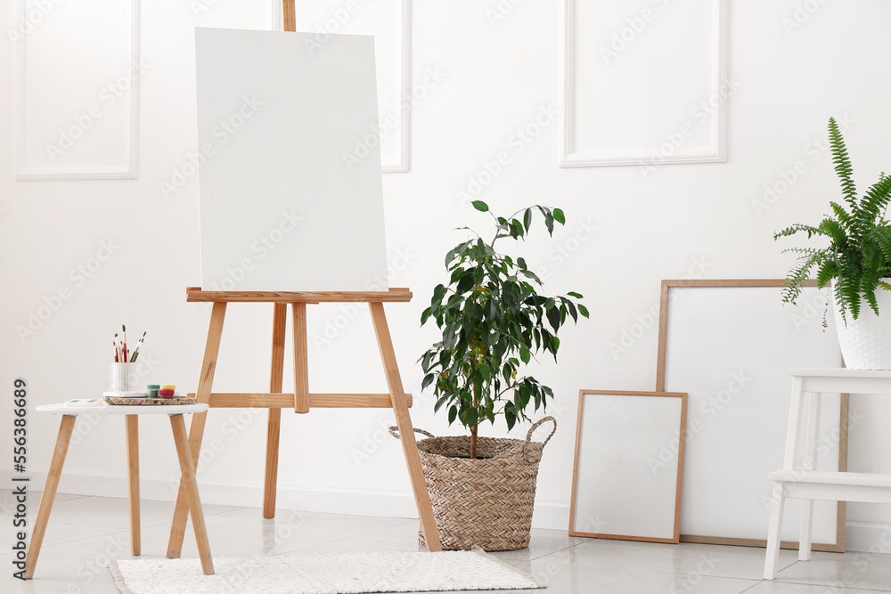 Interior of light room with easel, houseplants and blank frames