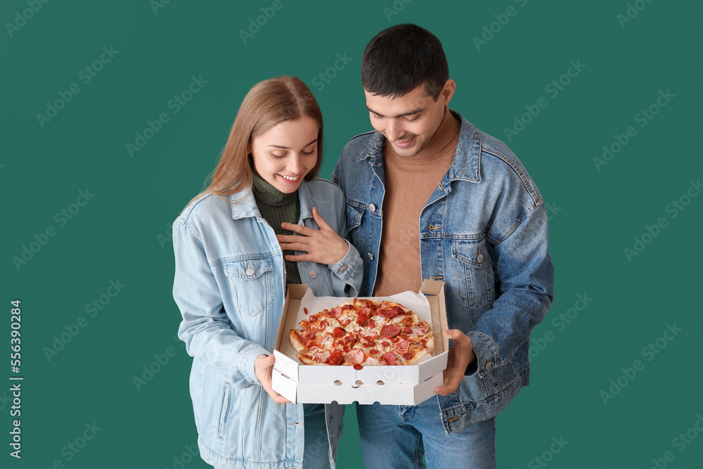 Happy young couple with fresh pizza on green background