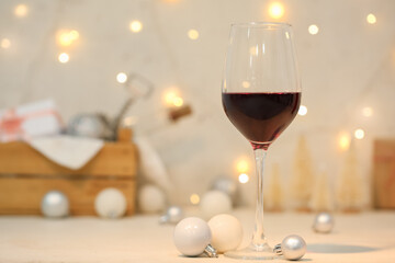 Glass of red wine with Christmas balls on light table, closeup