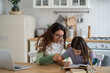 © DimaBerlin - Young mother wearing glasses helping schoolgirl daughter to do homework while sitting together at kitchen table. Teen girl child learning language with tutor at home. Homeschooling concept