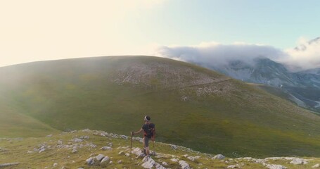 Wall Mural - young man hiker standing on ridge edge of the mountain in abruzzo italy with poles at sunset