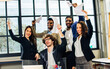 © Ann Rodchua - Group of diverse multiethnic businesspeople wearing formal suits, raising hands, smiling together with happiness and success, standing in modern indoor office after finishing teamwork project.