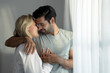 © Basicdog - Young Caucasian couple hugging and smiling warmly in bedroom at home.
