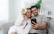 © Basicdog - Cheerful Caucasian man hugging his woman and looking at mobile phone screen.