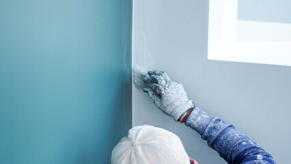 Wall Mural - A worker is painting the walls of the house with a primer using a paint roller.