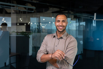 Portrait of african american businessman in office, man in shirt standing near window smiling and looking at camera, programmer working inside development company.