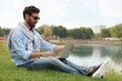 © New Africa - Man in sunglasses with laptop on green grass near lake