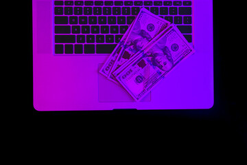 Wall Mural - Laptop and paper money in neon lighting, top view.